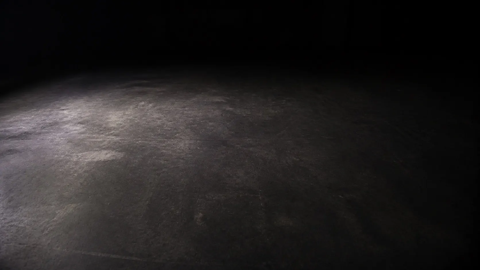 A bare dark training floor seen from standing height, stretching away into shadow.